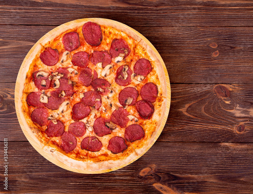 Salami pizza with mushrooms on bamboo bottom, on wooden table top view, space for text