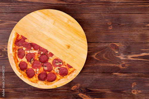 Half of salami pizza with mushrooms, on bamboo bottom, on wooden table, top view, space for text