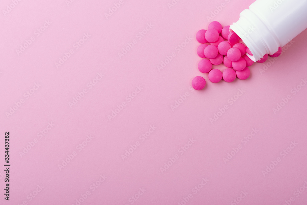Pills of bright pink color are scattered from a white medical jar. Isolated on a pink background. Pills of bright pink color are scattered from a white medical jar. Isolated on a pink background.