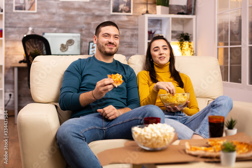 Beautiful young couple watching TV and eating fast food takeaway