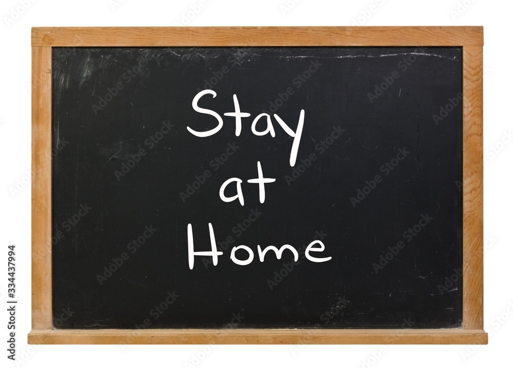 Fototapeta premium Stay at home written in white chalk on a black chalkboard isolated on white