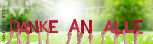 People Hands Holding Colorful German Word Danke An Alle Means Thank You All. Sunny Green Grass Meadow As Background photo