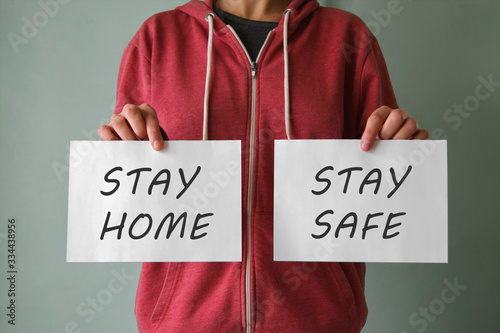 A young man is holding a papers with the words "Stay home" and "Stay fafe".