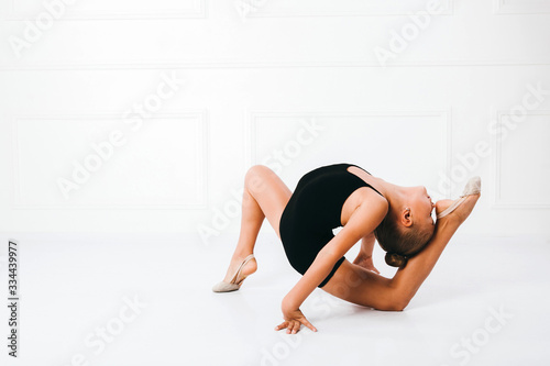 Young girl in a black dress doing gymnastics pose, forehead touches the heel, on white background