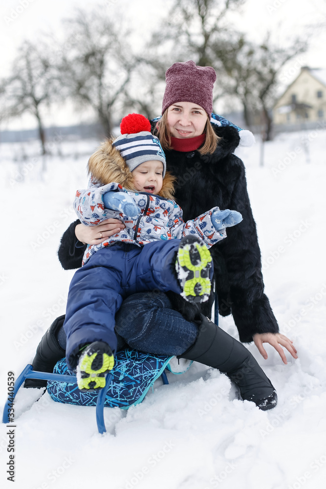 Smilling mother and her son sitting in the sledge in the winter garden.