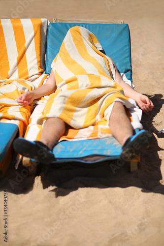 Portrait of a man who put a striped towel over himself not to bake in the sun on the sandy beach