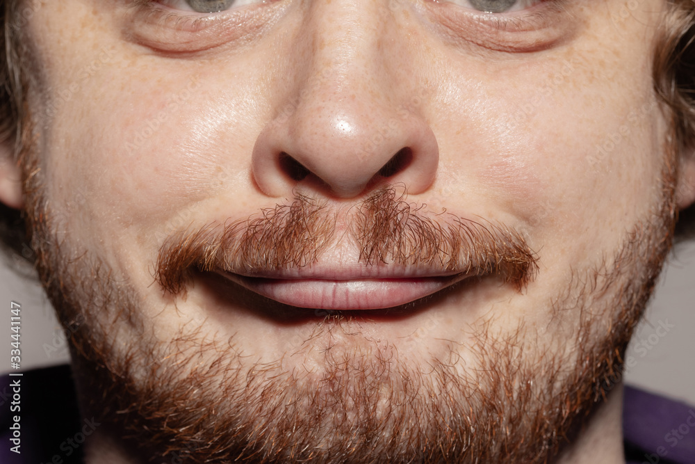 Grimaces. Close up of face of beautiful caucasian young man with redhair beard, focus on mouth. Human emotions, facial expression, cosmetology, body and skin care concept. Well kept skin. Wellbeing.