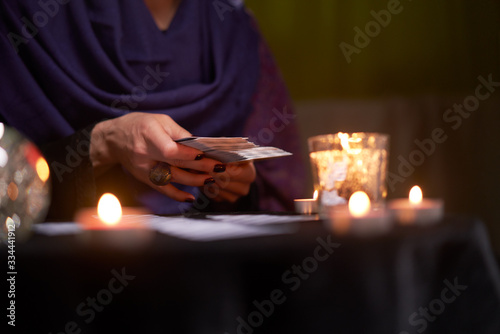 Close-up of soothsayer guessing on cards sitting at table with burning candles, magic ball