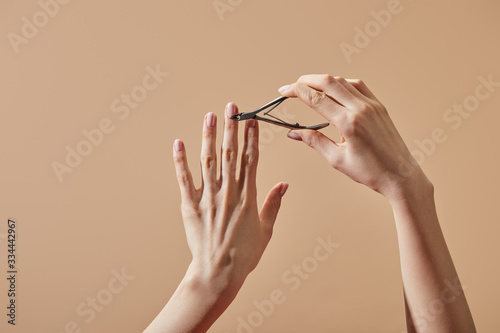 Partial view of woman doing manicure with cuticle nipper isolated on beige