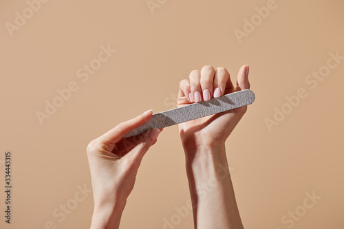 Photos Partial view of woman filing nails with emery board isolated on beige