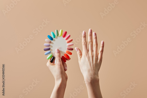 Valokuvatapetti Partial view of woman holding multicolored samples of nail polish isolated on be