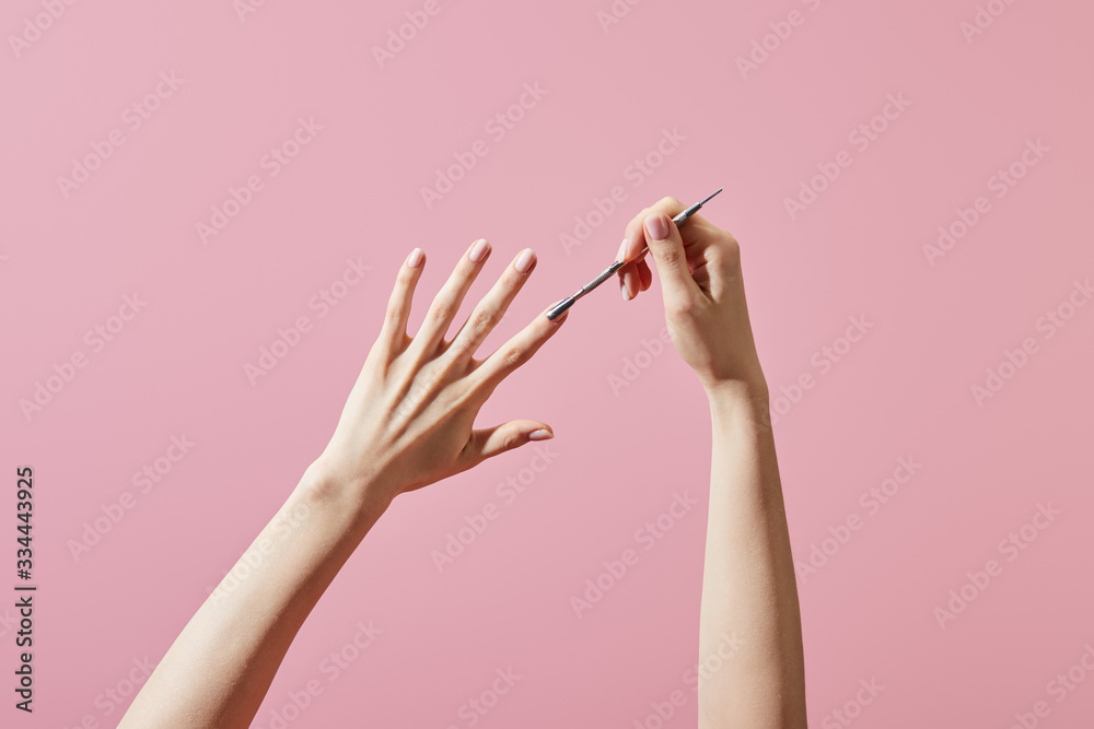 Cropped view of woman doing manicure with cuticle pusher isolated on pink - obrazy, fototapety, plakaty 