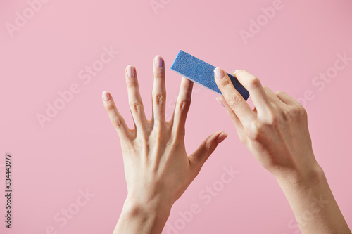 Partial view of woman doing manicure with nail buffer isolated on pink