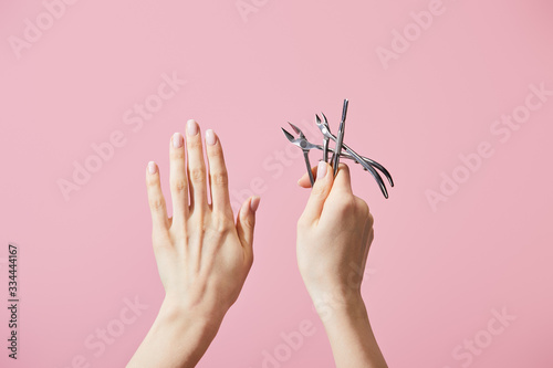Fotografie Cropped view of woman holding cuticle pusher and nippers isolated on pink