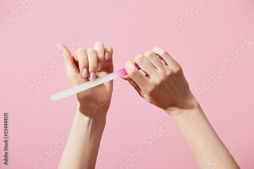 Cropped view of woman filing fingernail with nail file isolated on pink photo