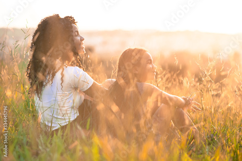 two afro american girls sitting on the field looking at the sunset.