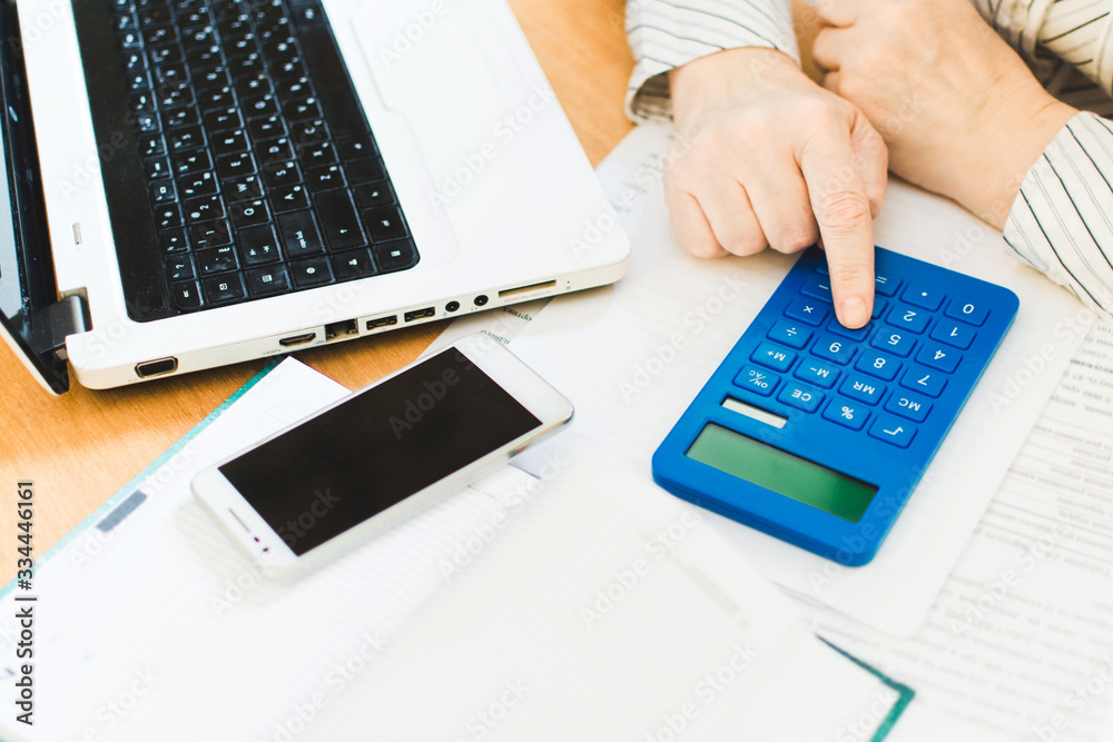 Social distancing protect coronavirus or covid-19. Closeup woman touching blue calculator. Female working in workplace at home. Accountant works remotely. Online education and distance work concept. Social distancing protect coronavirus or covid-19. Closeup woman touching blue calculator. Female working in workplace at home. Accountant works remotely. Online education and distance work concept.