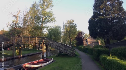 Pedestrian wooden bridge over a canal in Giethoorn, Netherlands. Little red boat standing in the river. In this city there are no cars.