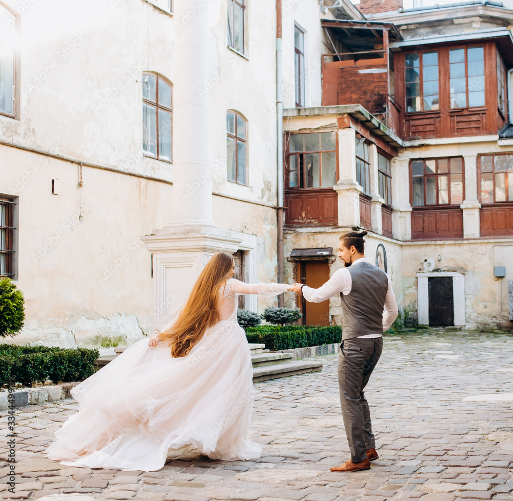 Happy newlyweds whirling, holding hands in old colorful yard Happy newlyweds whirling, holding hands in old colorful yard