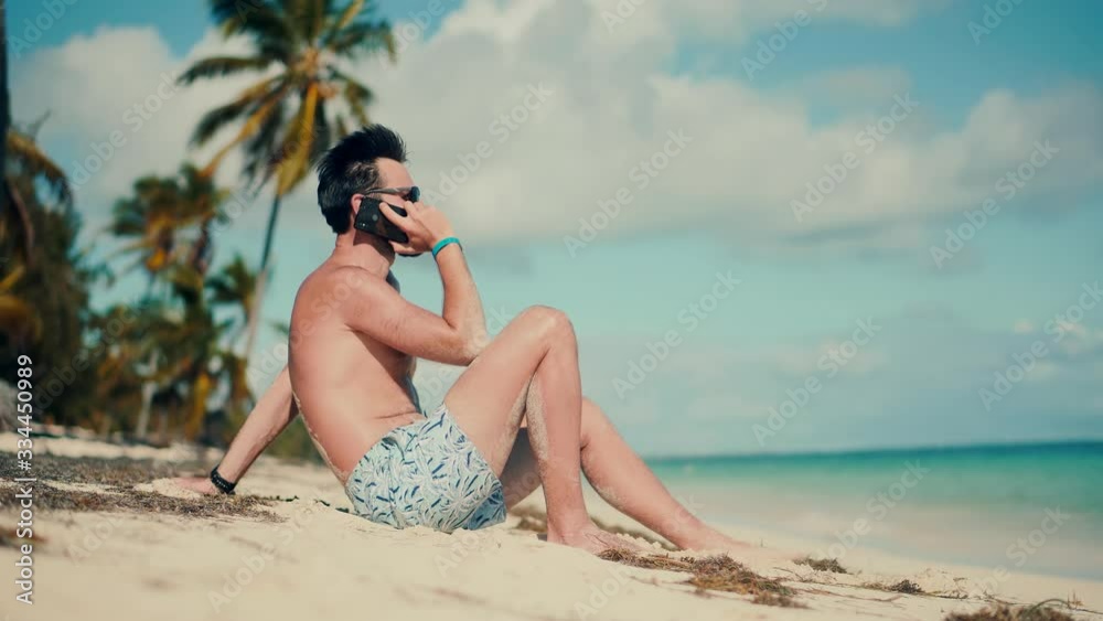 Businessman Working On Vacation.Man Sitting On Palm And Talking On Smartphone On Vacation Lounge Sea.Man Relaxing On Tropical Beach.Happy Calm Healthy Young Man Resting On Ocean And Hold Mobile Phone.