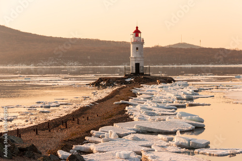 The famous Tokarevsky lighthouse on the Egersheld peninsula in Vladivostok on a winter morning at dawn among ice floes floating in the sea. photo