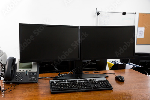 Workstation in modern office interior with dual black monitors on wooden desk close up