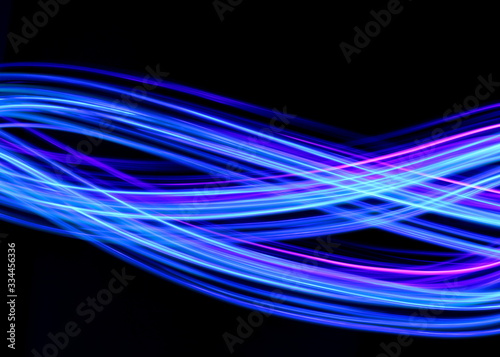 Long exposure photograph of neon blue streaks of light in an abstract swirl, parallel lines pattern against a black background. Light painting photography.