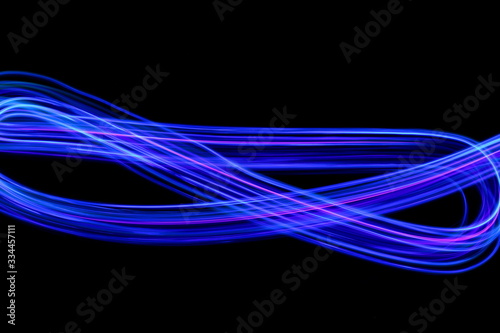 Long exposure photograph of neon blue streaks of light in an abstract swirl, parallel lines pattern against a black background. Light painting photography. © LizFoster