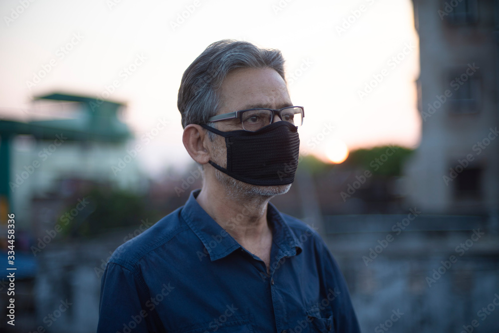 Portrait of an Indian old man wearing corona preventive mask on a rooftop in home isolation.Indian lifestyle, disease and home quarantine. Portrait of an Indian old man wearing corona preventive mask on a rooftop in home isolation.Indian lifestyle, disease and home quarantine.