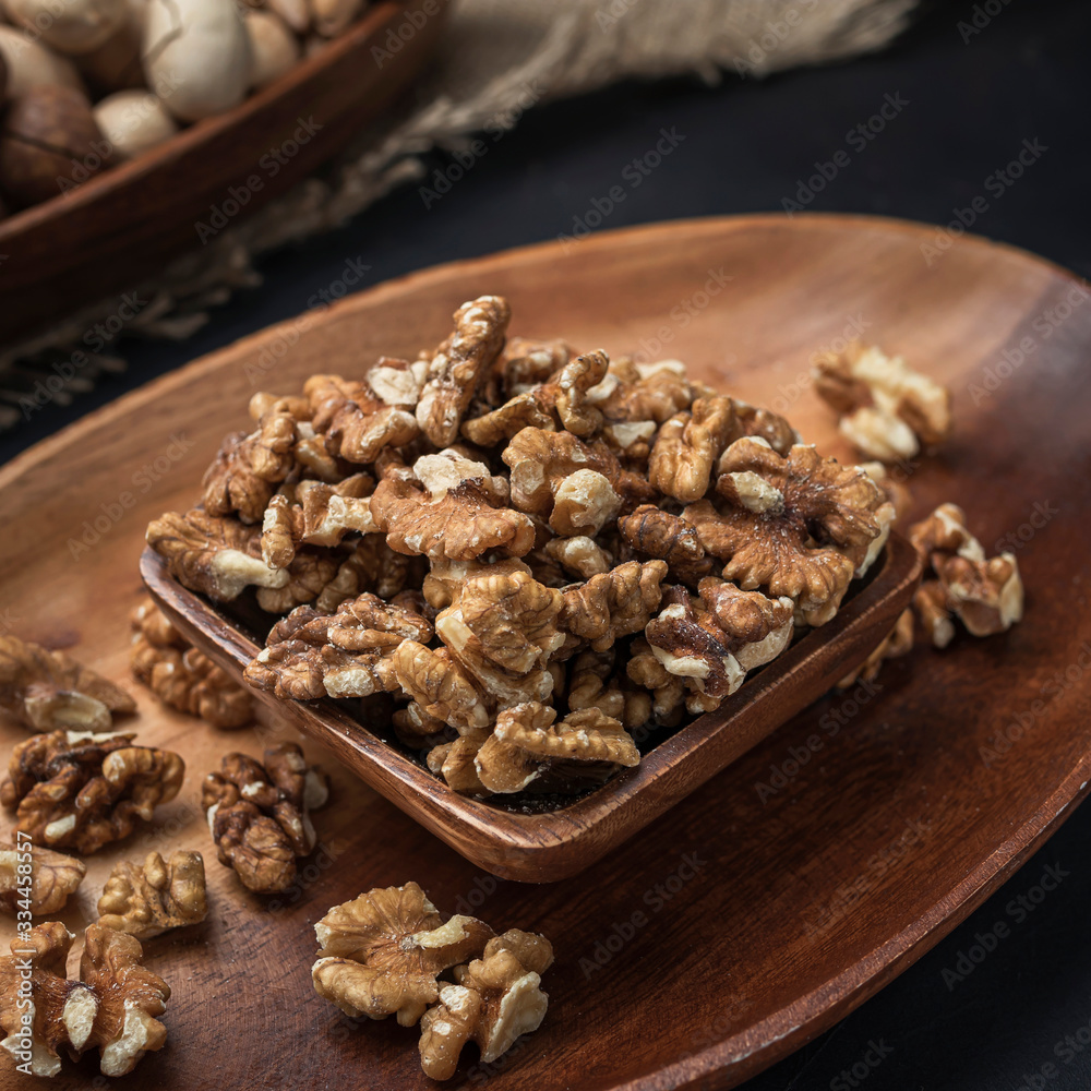 nuts on a square wooden bowl and an oval wooden tray on a dark background and burlap