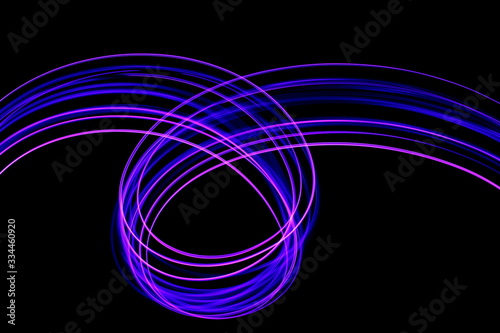 Long exposure photograph of neon purple streaks of light in an abstract swirl, parallel lines pattern against a black background. Light painting photography.