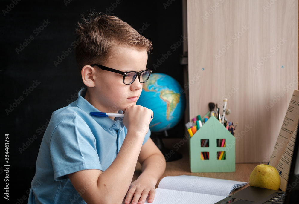 a cute boy takes an online education course at home at a table in front ...