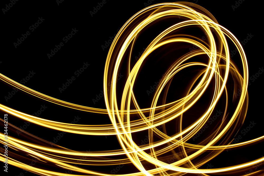 Long exposure photograph of neon gold streaks of light in an abstract swirl, parallel lines pattern against a black background. Light painting photography. Long exposure photograph of neon gold streaks of light in an abstract swirl, parallel lines pattern against a black background. Light painting photography.