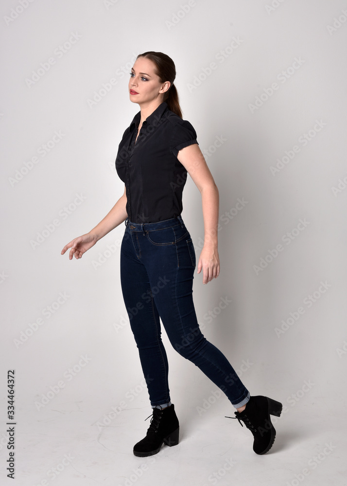 Portrait of a pretty brunette girl with ponytail, wearing jeans boots and a black blouse. full length standing pose on a studio background. Portrait of a pretty brunette girl with ponytail, wearing jeans boots and a black blouse. full length standing pose on a studio background.
