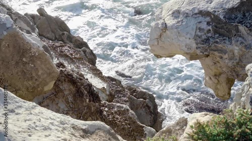 Shot from above and between rocks with ocean waves breaking in the background.