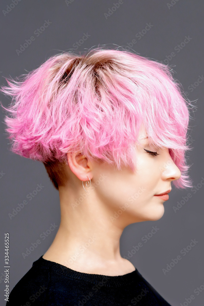 Woman with pink hairstyle stands with closed eyes side view on gray background with copy space. Woman with pink hairstyle stands with closed eyes side view on gray background with copy space.