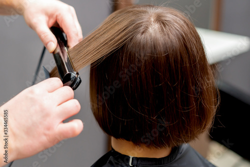 Hairdresser straightens hair of woman with hair straightener tool in hair salon.