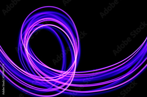 Long exposure photograph of neon purple streaks of light in an abstract swirl  parallel lines pattern against a black background. Light painting photography.