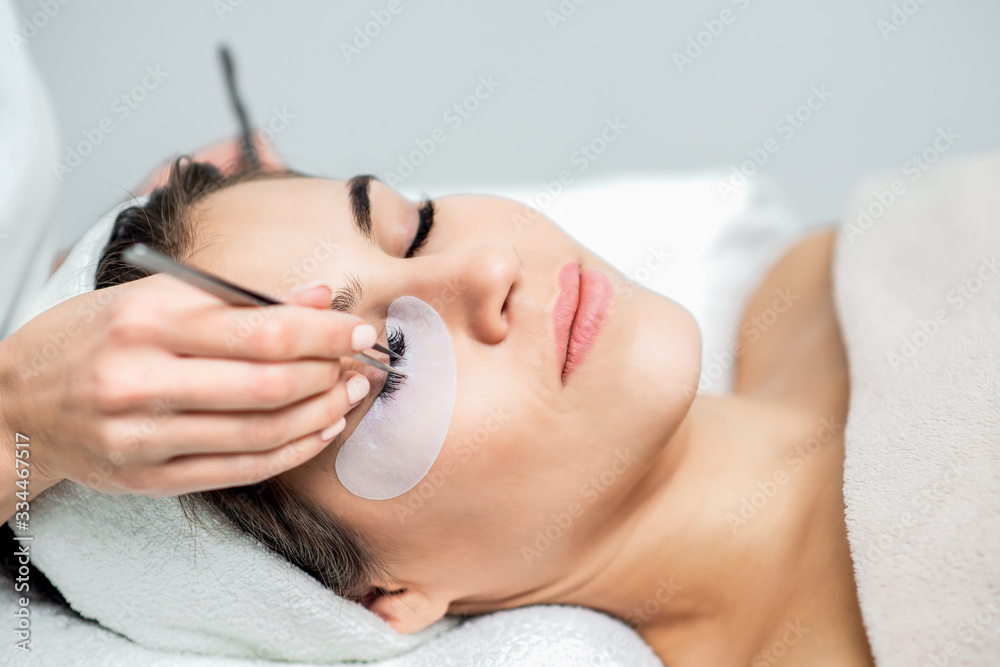 Young woman receiving eyelash extension procedure in beauty salon.
