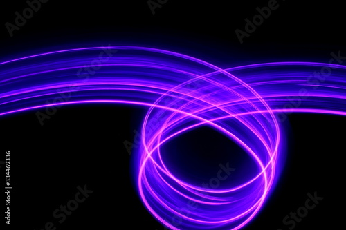 Long exposure photograph of neon purple streaks of light in an abstract swirl, parallel lines pattern against a black background. Light painting photography.