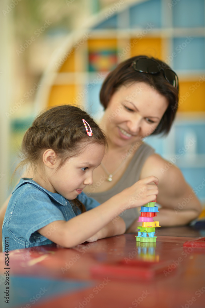 Little daughter and mother playing with colorful plastic blocks at home