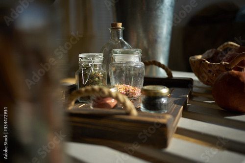spices in glass jars are placed on a wooden tray. light from the window