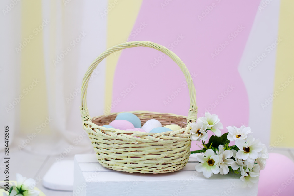 Basket of colorful easter eggs with flowers. Wicker yellow basket with Easter eggs on color background. View with copy space. basket with easter eggs and daisies on a wooden table. Spring decor. Farm