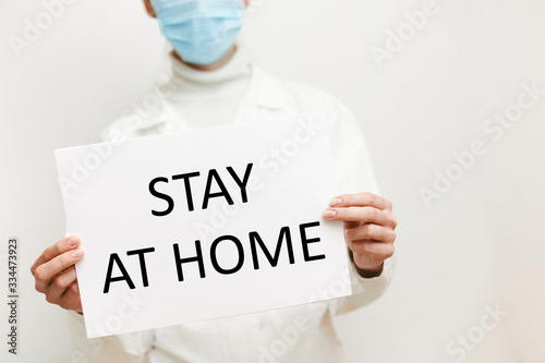 Stay At Home sign. Physician woman shows warning inscription Stay At Home at white name plate. Covid-19 protection measures. Quarantine or self isolation warning