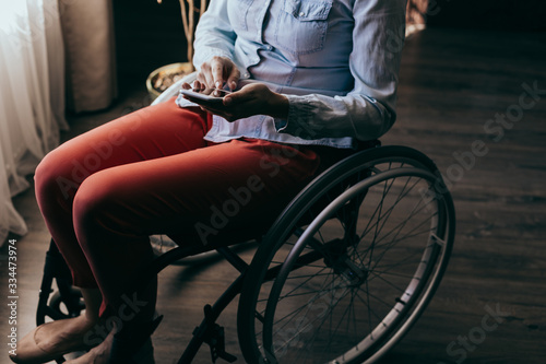 close up of a young woman in a wheelchair with a mobile phone in her hands at home. Recovery and healthcare concepts.
