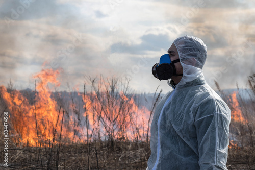 Portrait of a man in a white chemical protective suit and a respirator against the background of a forest fire. Concept of environmental, chemical, epidemic and radiation problems.