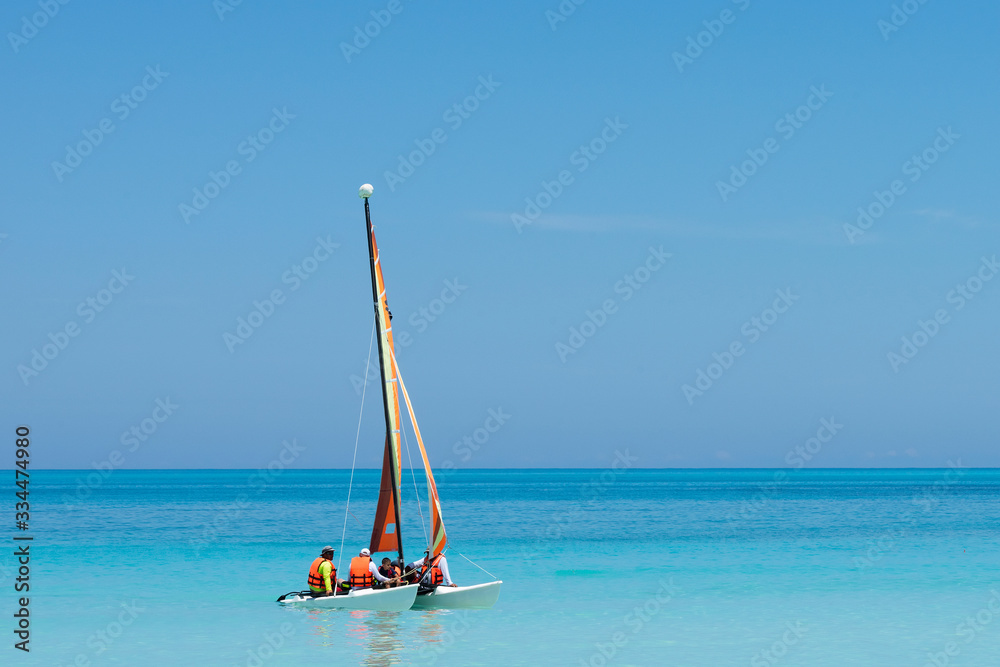 Naklejka premium a colorful and beautiful catamaran sails the turquoise blue waters with tourists in the clear waters of cuba