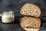 Sliced bread with jar of flour on a black background, two halves of wheat bread. Traditional wheat freshly rustic baked bread.