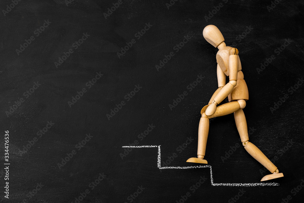 Wooden business man climbs the steps drawn on a chalk board