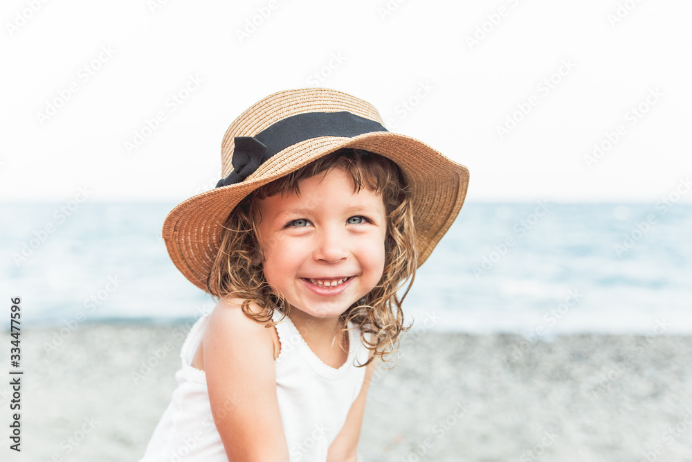 Portrait of happy child girl in hat on the beach with sea view.Vacation,summer concept